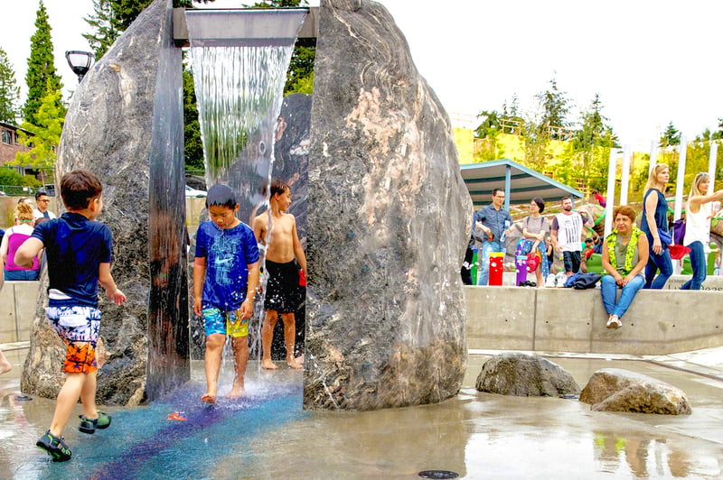 A boy walks through the waterfall feature between two “boulders” at universally accessible Inspiration Park in Bellevue, WA, USA.