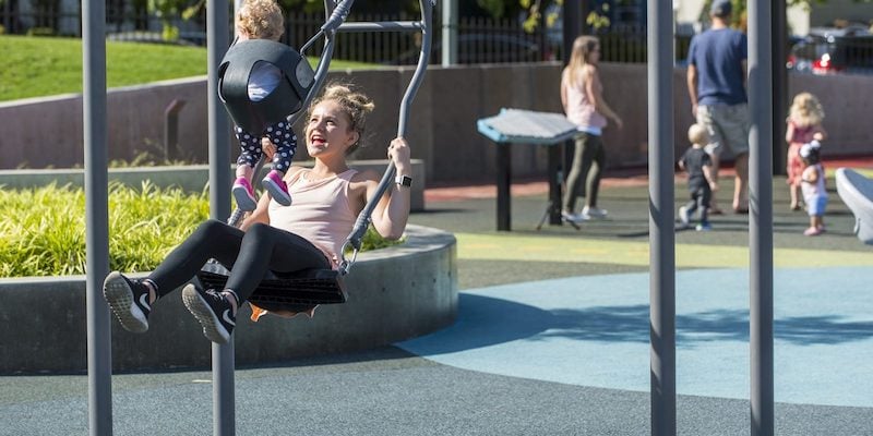 A woman enjoys the two-way swing with a baby at Let’s All Play Park, a multigenerational park located at Salem Health Hospital in Salem, OR, USA.